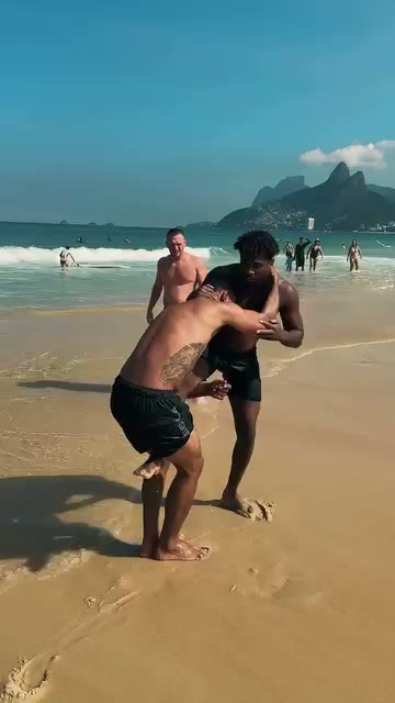 Two OSS Rio Tour travelers drilling Jiu-Jitsu on the sand in Rio de Janeiro, with Dois Irmãos behind them