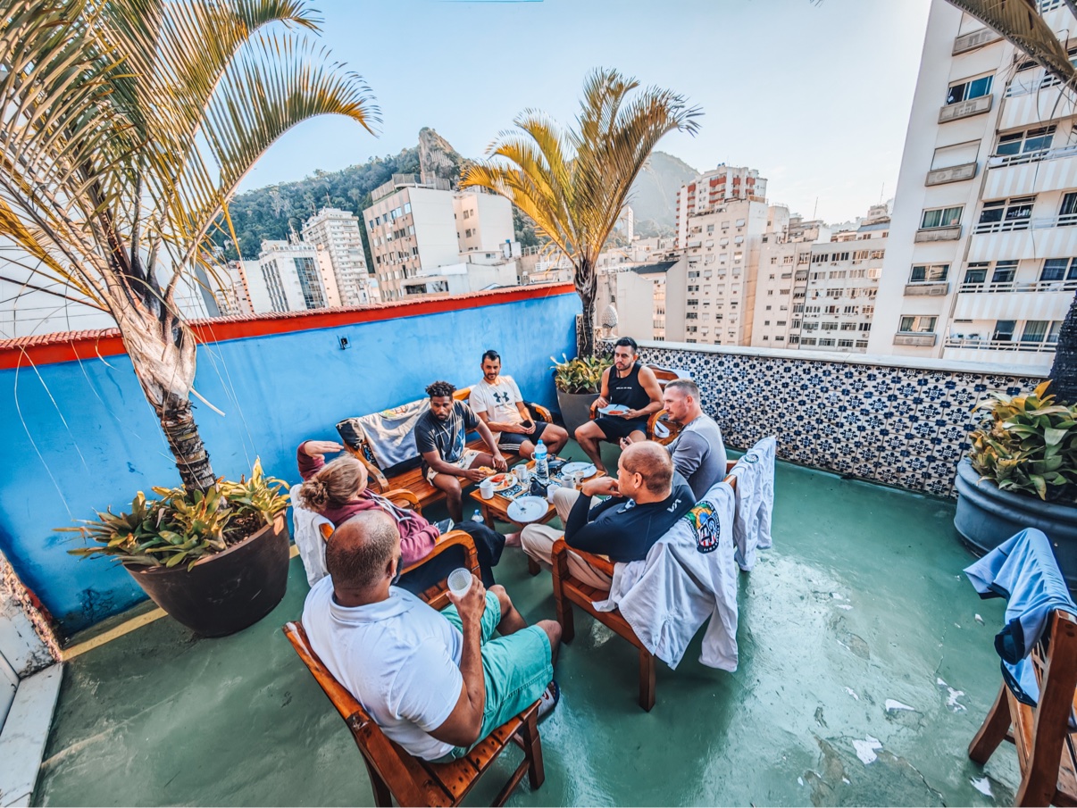 OSS Rio Tour travelers eating together on the Copacabana rooftop terrace, palm trees overhead and gis draped over the chairs