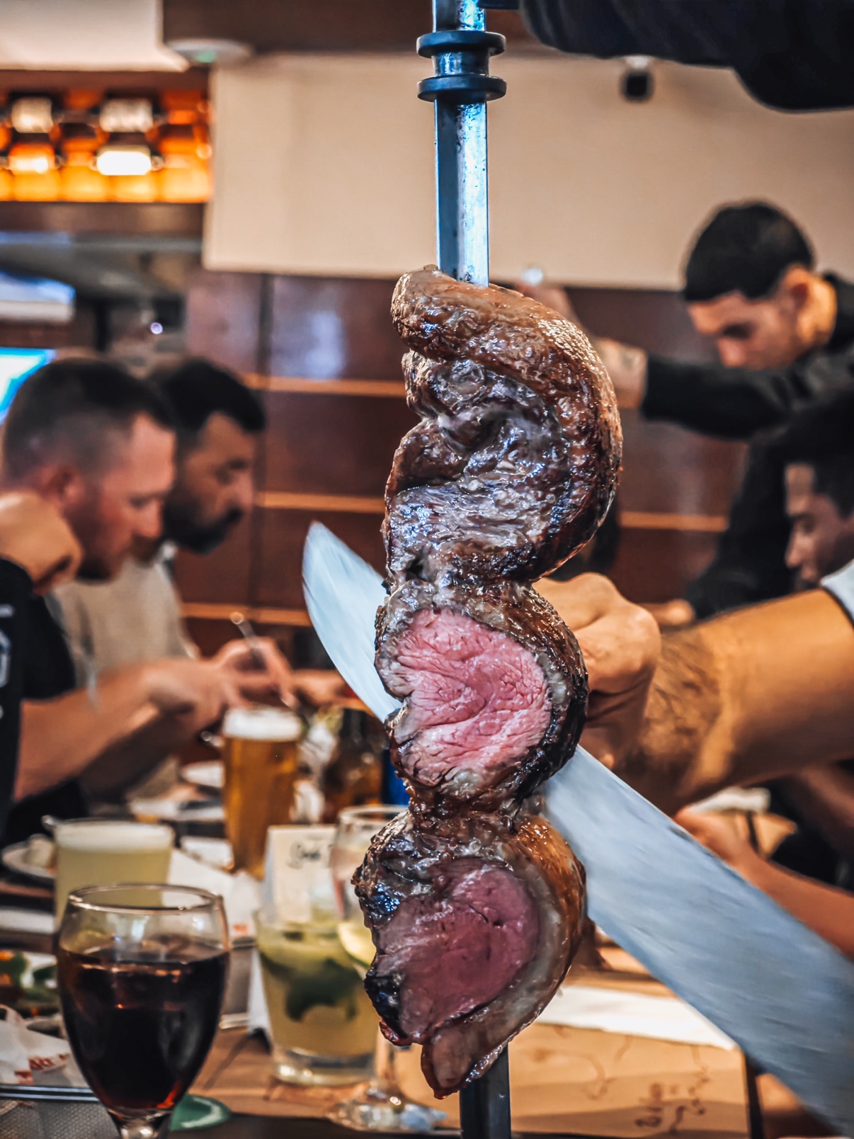 Picanha being carved off the skewer at the table of a Brazilian churrascaria while the OSS Rio Tour crew eats together